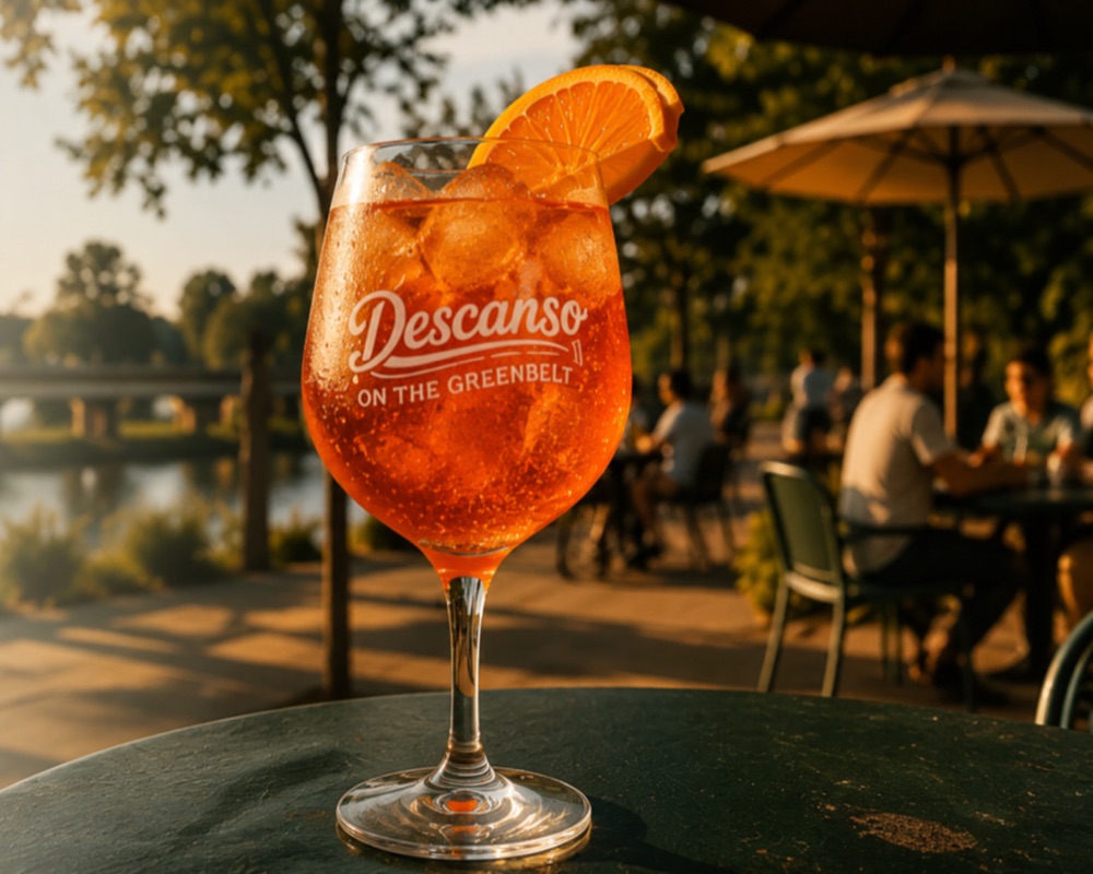 A Descanso-branded Aperol spritz at golden hour with the Greenbelt and patio in the background.